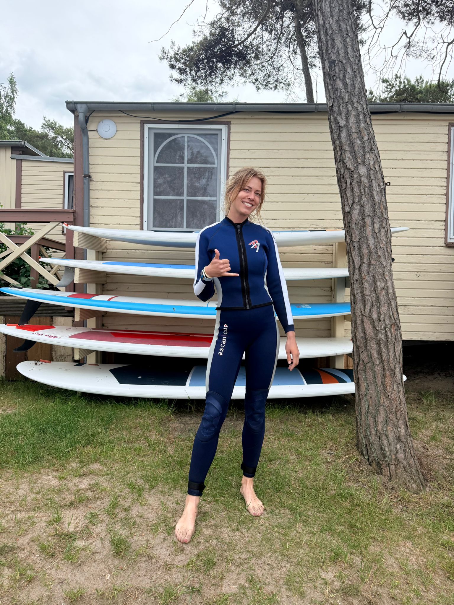 Laura mit Surf-/SUP-Anzug vor einem Board-Regal